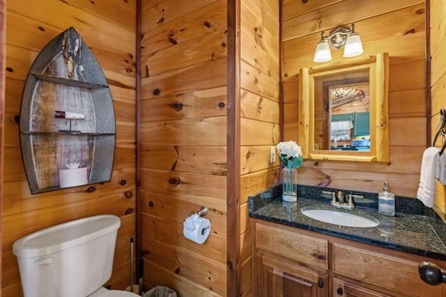 half bathroom featuring toilet, wood walls, and vanity