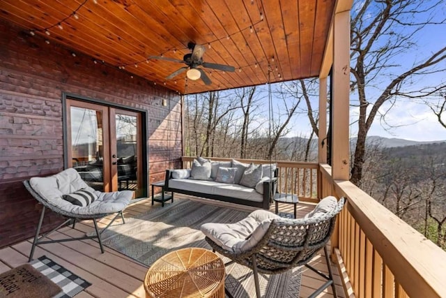 deck featuring a ceiling fan, a wooded view, french doors, and an outdoor hangout area