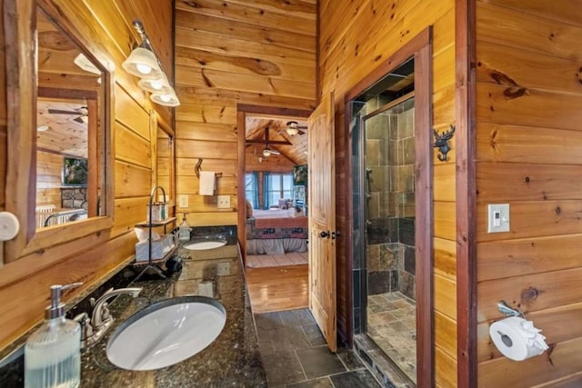 ensuite bathroom featuring a shower stall, stone finish flooring, wood walls, ensuite bathroom, and a sink