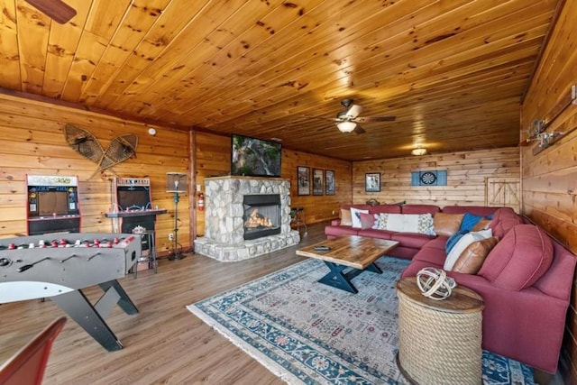living room with a stone fireplace, wooden ceiling, a ceiling fan, and wood finished floors