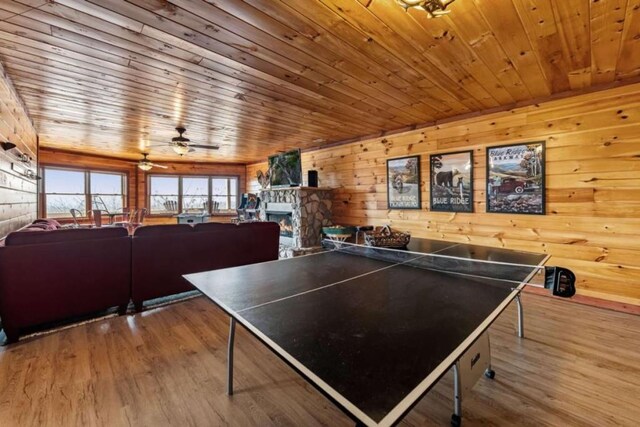 rec room with a stone fireplace, wooden ceiling, wood finished floors, and ceiling fan