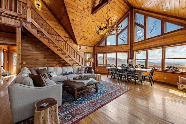 living area with wooden walls, stairway, wood ceiling, an inviting chandelier, and wood finished floors