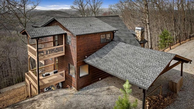 exterior space with a chimney, a shingled roof, and a balcony