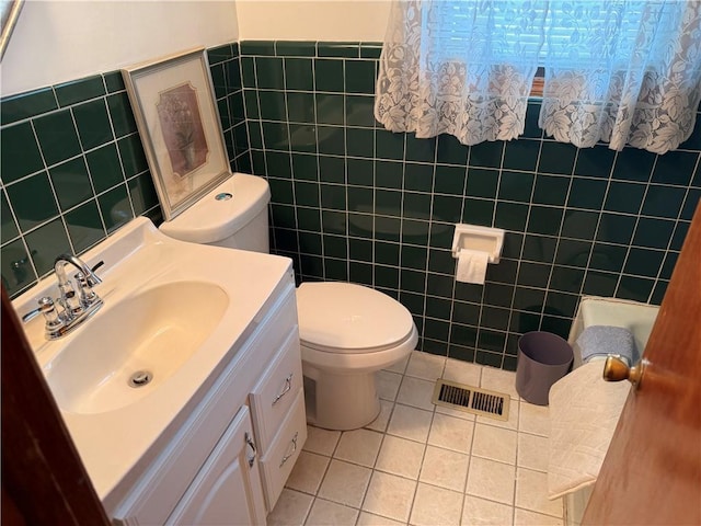 half bath with tile walls, tile patterned floors, toilet, vanity, and a wainscoted wall