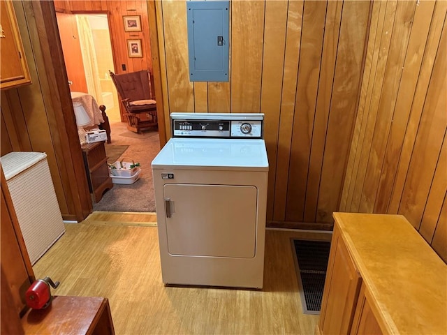 laundry room with washer / dryer, electric panel, wood walls, light wood finished floors, and cabinet space