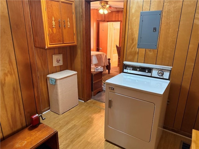 laundry room featuring electric panel, cabinet space, wood walls, a ceiling fan, and light wood-style floors