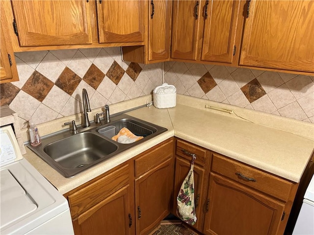 kitchen with a sink, washer / clothes dryer, light countertops, and brown cabinetry