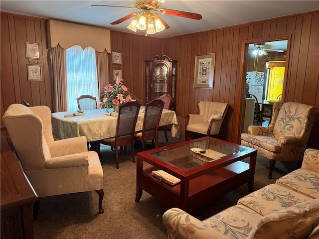 living area featuring a ceiling fan, carpet, wood walls, and ornamental molding