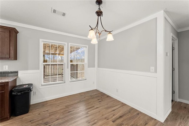 unfurnished dining area with crown molding, a notable chandelier, visible vents, wainscoting, and light wood-type flooring