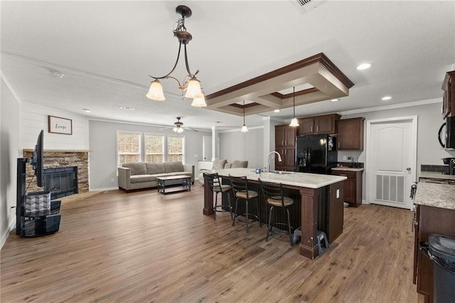 kitchen featuring a sink, wood finished floors, dark brown cabinets, black appliances, and a kitchen bar