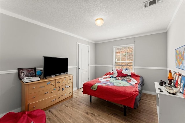 bedroom featuring a textured ceiling, light wood finished floors, visible vents, and crown molding