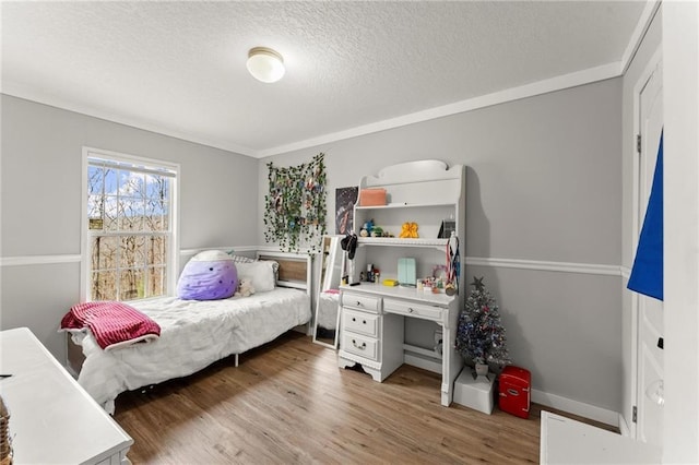 bedroom featuring crown molding, a textured ceiling, baseboards, and wood finished floors