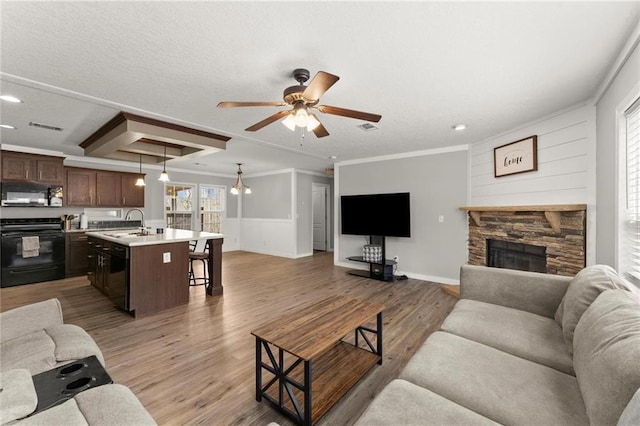 living room with a fireplace, crown molding, visible vents, light wood-style flooring, and ceiling fan