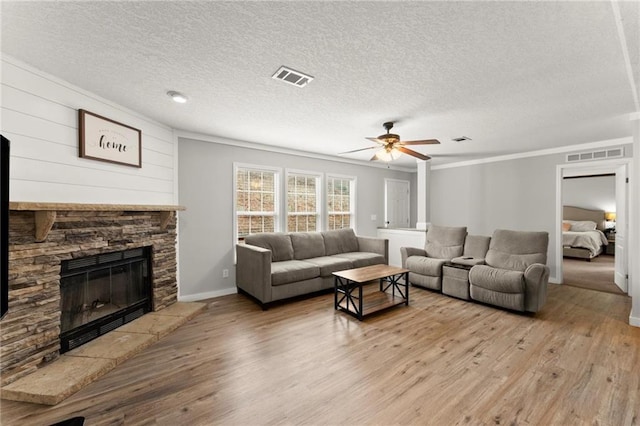 living area with visible vents, a stone fireplace, baseboards, and wood finished floors