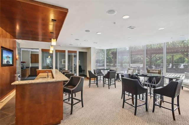 dining room featuring light carpet, floor to ceiling windows, and wooden walls