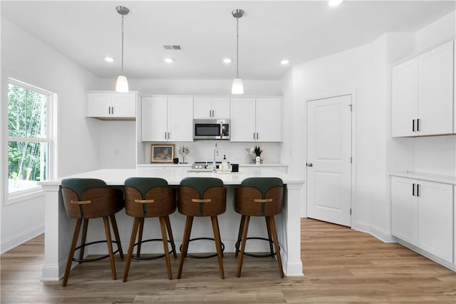 kitchen featuring stainless steel microwave, white cabinetry, visible vents, and a kitchen island with sink