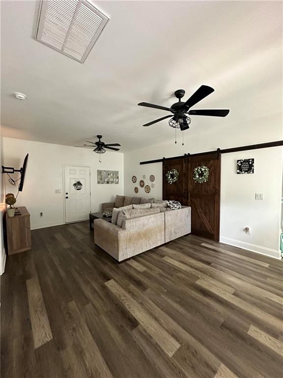 unfurnished bedroom featuring dark wood-type flooring, a barn door, and ceiling fan