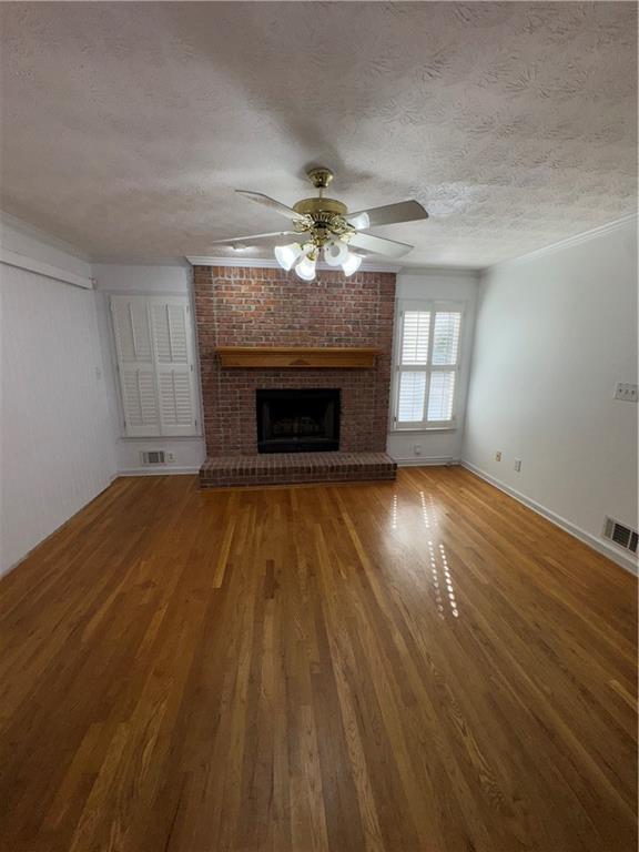 unfurnished living room with ceiling fan, hardwood / wood-style floors, a textured ceiling, and a brick fireplace