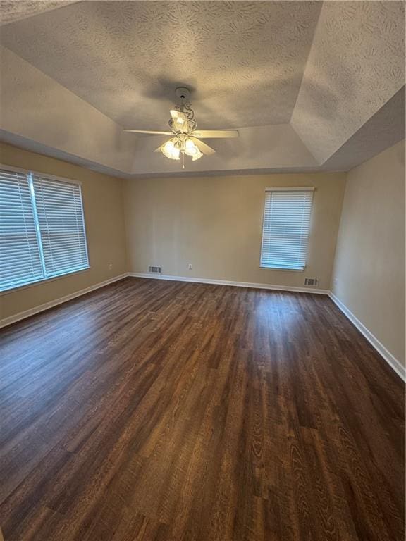 empty room with ceiling fan, dark wood-type flooring, a raised ceiling, and a textured ceiling