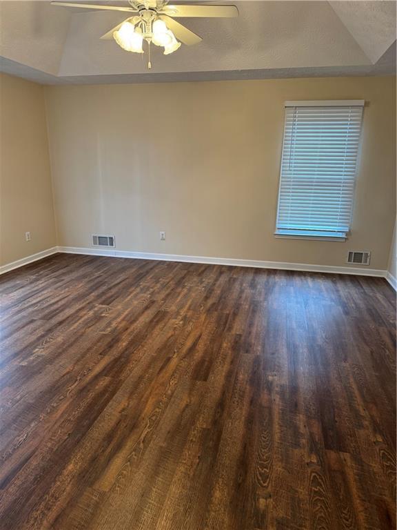 unfurnished room featuring a raised ceiling, ceiling fan, dark hardwood / wood-style flooring, and a textured ceiling