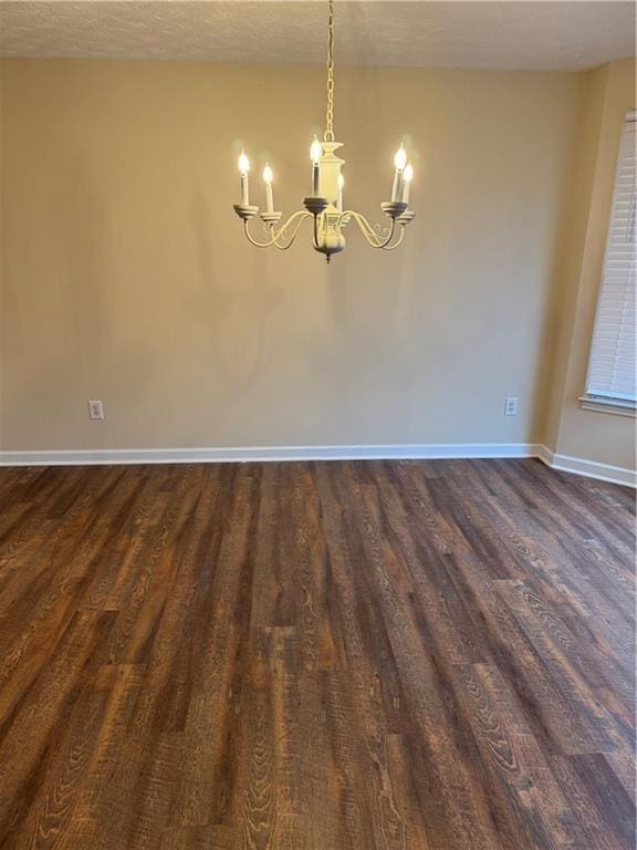 spare room with an inviting chandelier and dark hardwood / wood-style floors