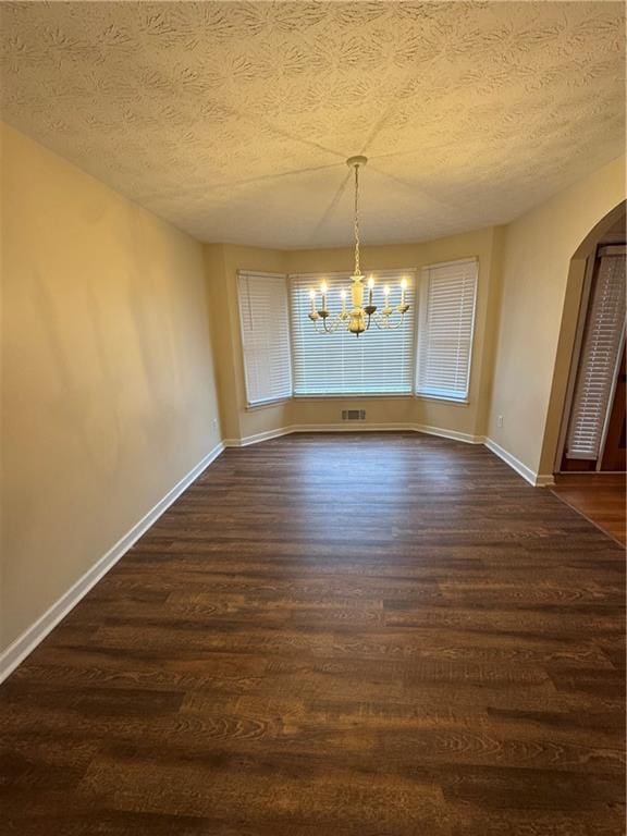 unfurnished dining area with a notable chandelier, dark hardwood / wood-style floors, and a textured ceiling