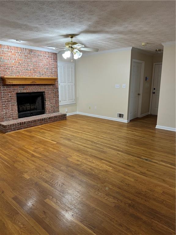 unfurnished living room featuring ornamental molding, wood-type flooring, a brick fireplace, and a textured ceiling