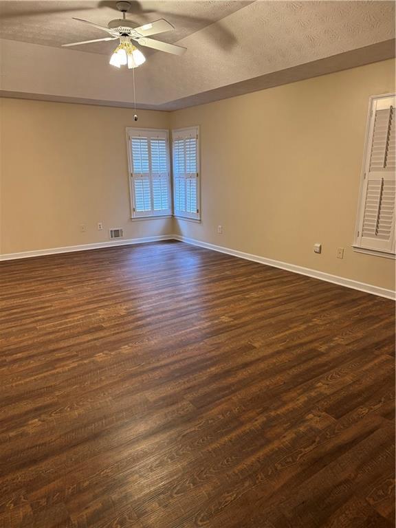 empty room with a textured ceiling, ceiling fan, and dark hardwood / wood-style flooring