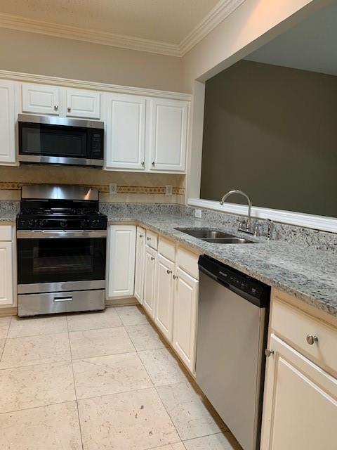 kitchen with sink, white cabinetry, stainless steel appliances, ornamental molding, and light stone countertops