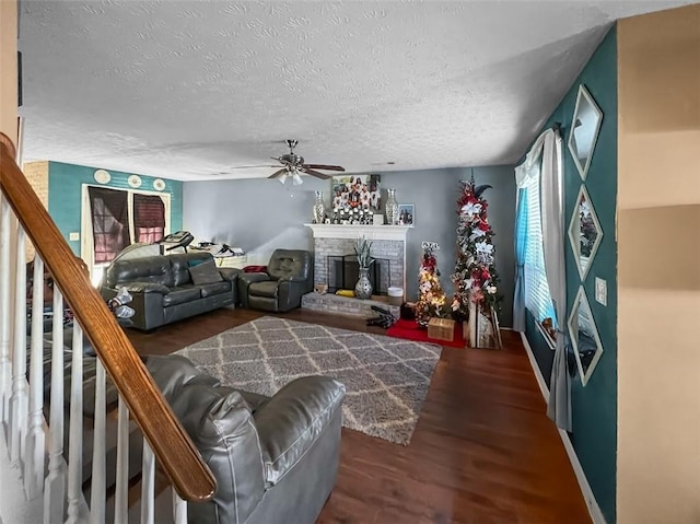 living area with ceiling fan, wood finished floors, stairs, a textured ceiling, and a brick fireplace