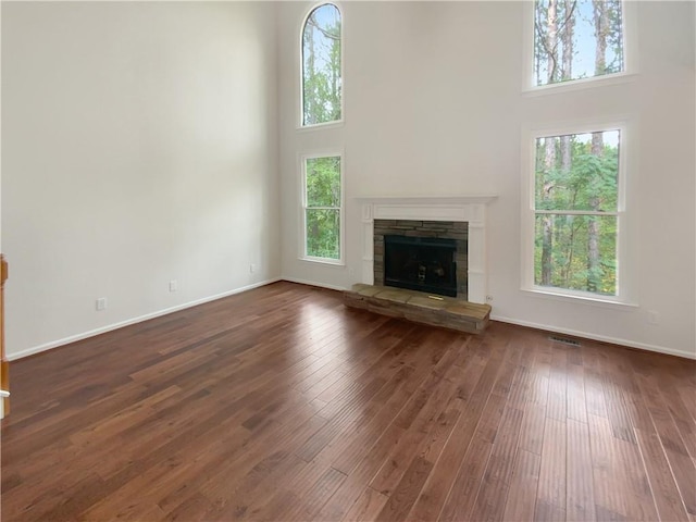 unfurnished living room featuring a stone fireplace, a high ceiling, dark hardwood / wood-style flooring, and a healthy amount of sunlight