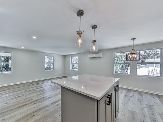 kitchen featuring gray cabinetry, hanging light fixtures, light hardwood / wood-style flooring, light stone counters, and a wall unit AC