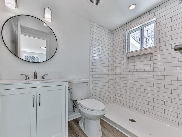 bathroom featuring hardwood / wood-style flooring, vanity, toilet, and tiled shower