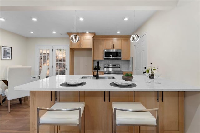 kitchen with a breakfast bar, tasteful backsplash, sink, light hardwood / wood-style floors, and stainless steel appliances