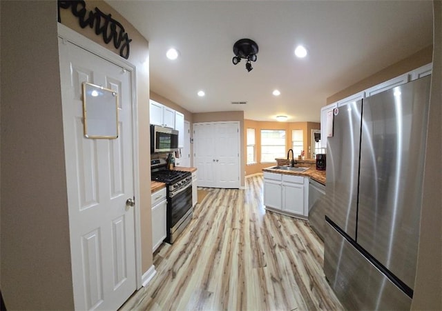 kitchen featuring butcher block counters, sink, light hardwood / wood-style flooring, white cabinetry, and stainless steel appliances