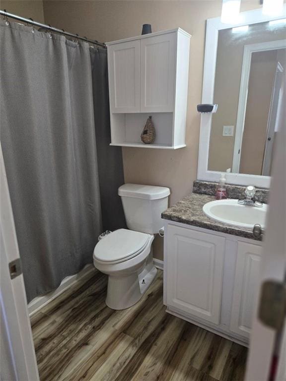 bathroom with hardwood / wood-style floors, vanity, toilet, and walk in shower