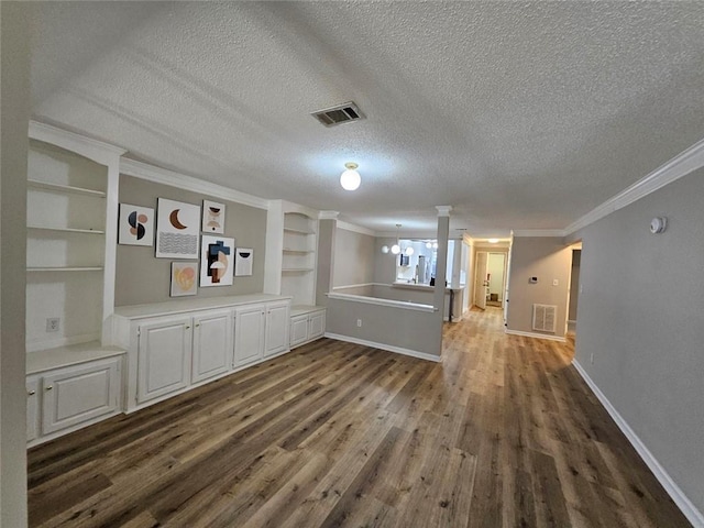 interior space featuring a chandelier, a textured ceiling, ornamental molding, dark hardwood / wood-style floors, and decorative columns