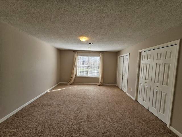 unfurnished bedroom with multiple closets, carpet flooring, and a textured ceiling