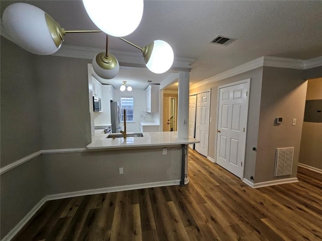 kitchen featuring dark wood-type flooring, white cabinetry, stainless steel appliances, ornamental molding, and kitchen peninsula