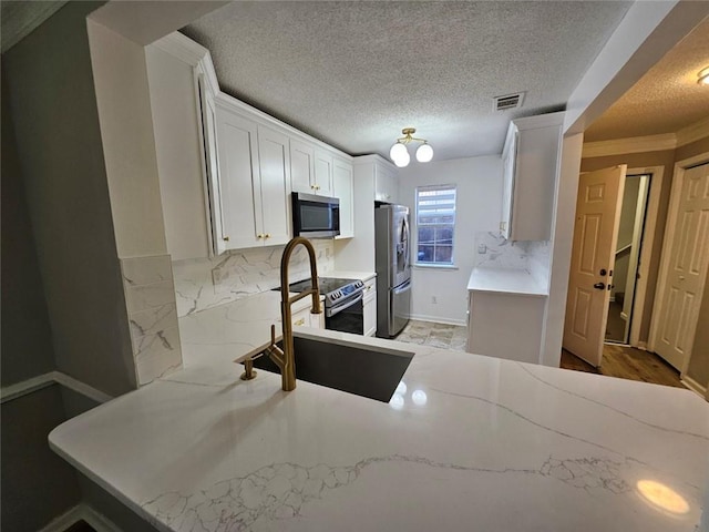 kitchen with appliances with stainless steel finishes, white cabinetry, sink, backsplash, and kitchen peninsula