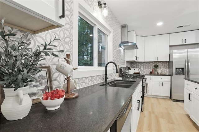 kitchen featuring sink, white cabinets, light hardwood / wood-style floors, stainless steel appliances, and wall chimney range hood