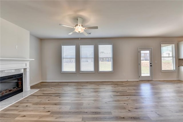 unfurnished living room featuring ceiling fan, a high end fireplace, and light wood-type flooring