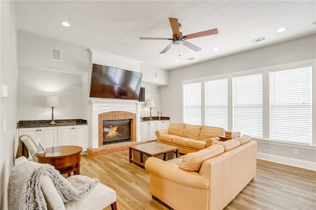 living room with light hardwood / wood-style floors, a brick fireplace, and ceiling fan