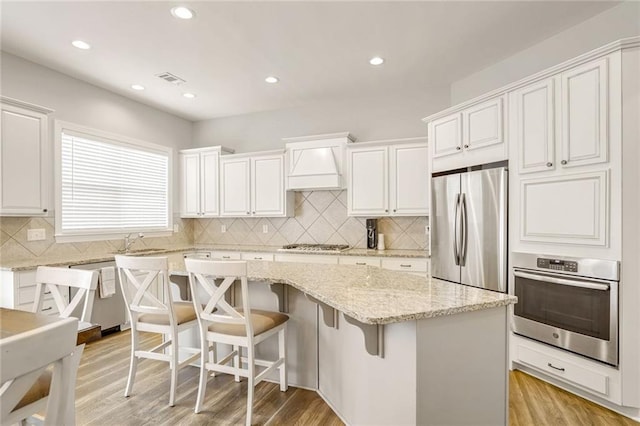 kitchen with white cabinets, appliances with stainless steel finishes, a kitchen bar, a kitchen island, and light wood-type flooring