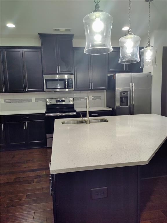 kitchen featuring appliances with stainless steel finishes, decorative light fixtures, dark wood-type flooring, and sink