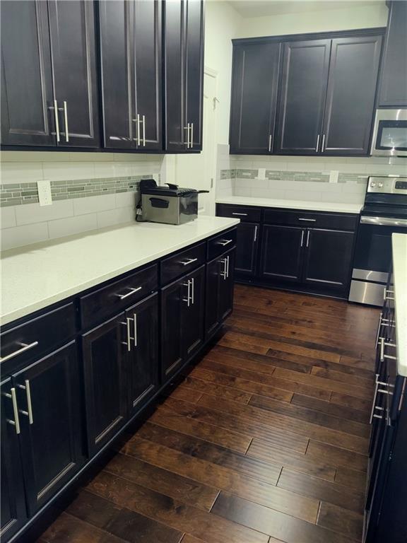 kitchen with dark hardwood / wood-style flooring, stainless steel appliances, and tasteful backsplash