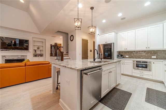 kitchen featuring sink, stainless steel appliances, decorative light fixtures, a center island with sink, and white cabinets