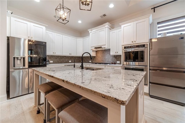 kitchen featuring white cabinetry, hanging light fixtures, appliances with stainless steel finishes, and an island with sink