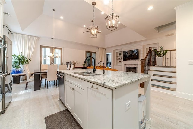 kitchen with a center island with sink, sink, decorative light fixtures, light stone counters, and white cabinetry