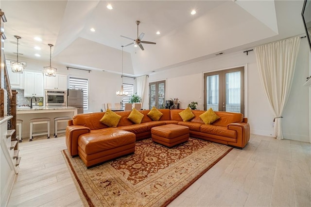 living room featuring a healthy amount of sunlight, high vaulted ceiling, light hardwood / wood-style floors, and ceiling fan with notable chandelier